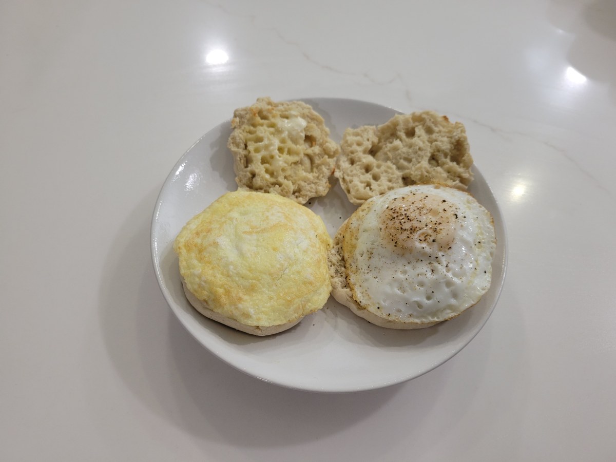 Two English muffins on a white plate, top halves off. Left: a scrambled egg formed into a round patty on the muffin bottom. Right: a sunny-side up egg on the muffin bottom. Toasted, buttered muffin tops beside each.