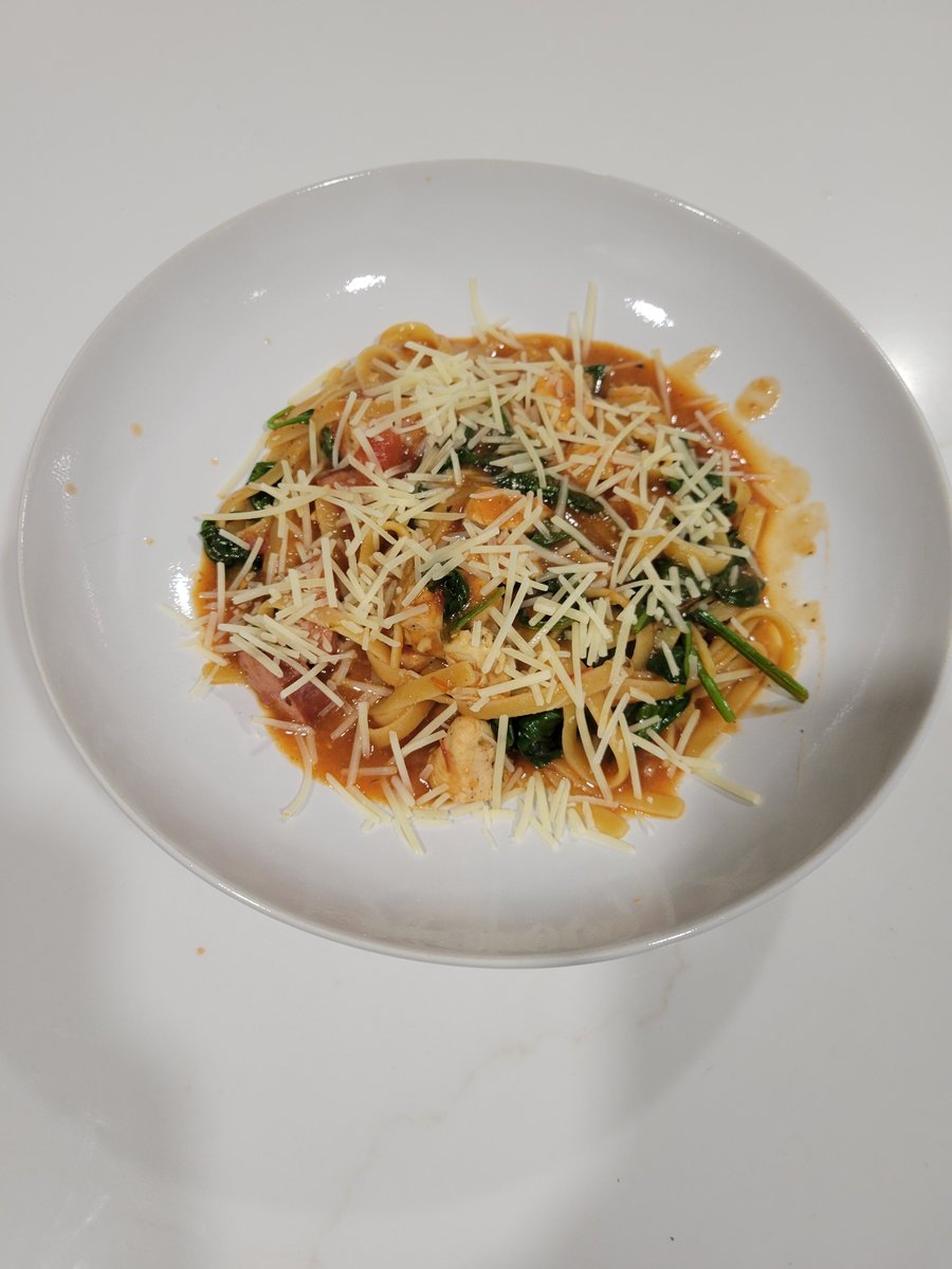 A bowl of one-pot pasta with chicken, spinach, and tomatoes covered in melted Parmesan