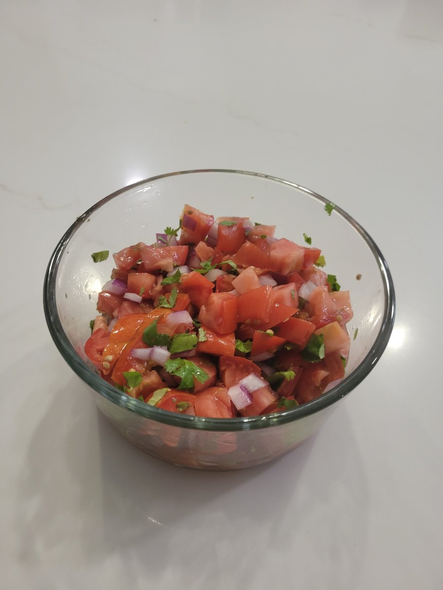 A glass bowl of finished pico de gallo with diced Roma tomatoes, red onion, and chopped cilantro