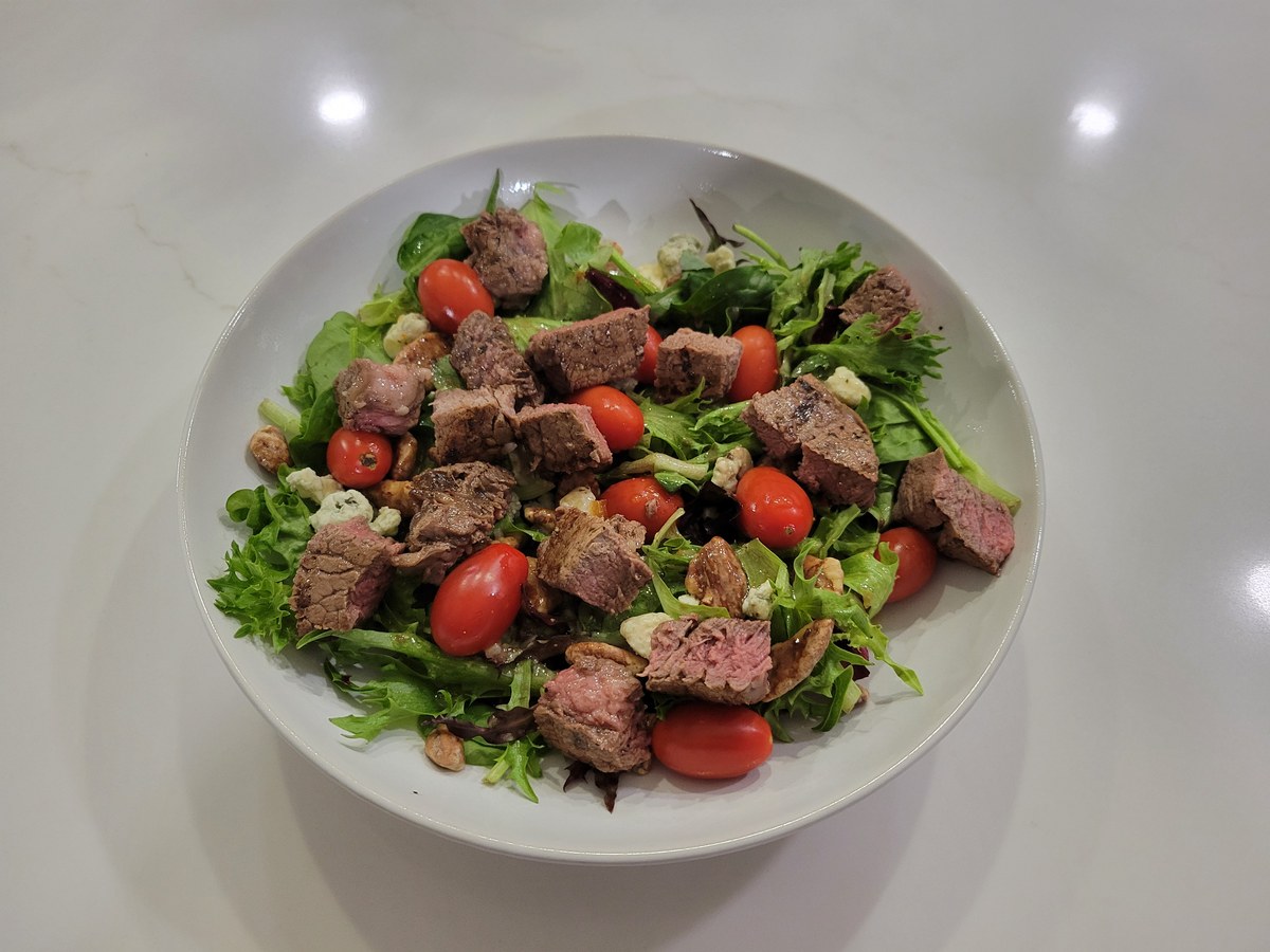 A steakhouse salad: diced steak over spring mix with blue cheese, glazed pecans, and grape tomatoes (whole, not halved).
