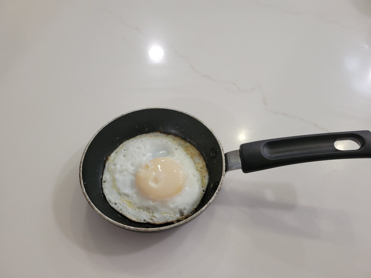 A single sunny-side-up egg in a small nonstick skillet, whites fully set and opaque with no runny patches, yolk covered with a thin opaque film indicating the whites are done and the yolk is still liquid inside